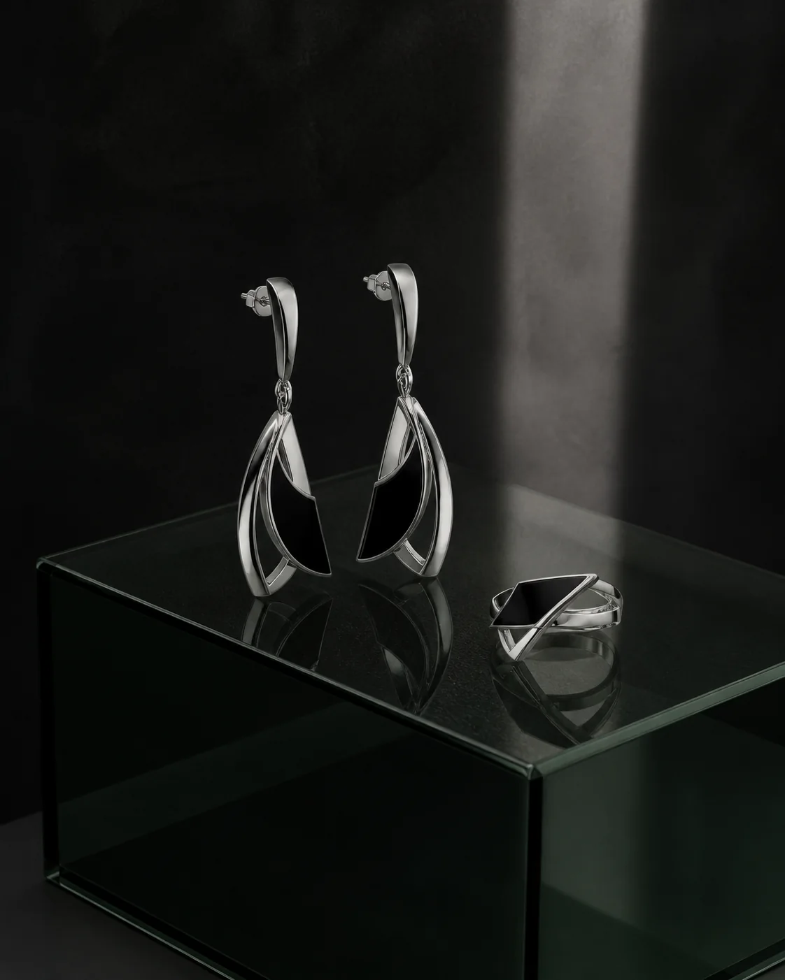 Detailed silver earrings and ring on a dark plinth